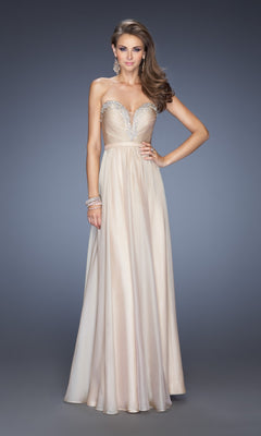 A woman wears the La Femme Designer Pleated Chiffon Prom Dress 20027, a strapless champagne gown with a jeweled bodice and sweetheart neckline, floor-length, shown against a plain gray background.