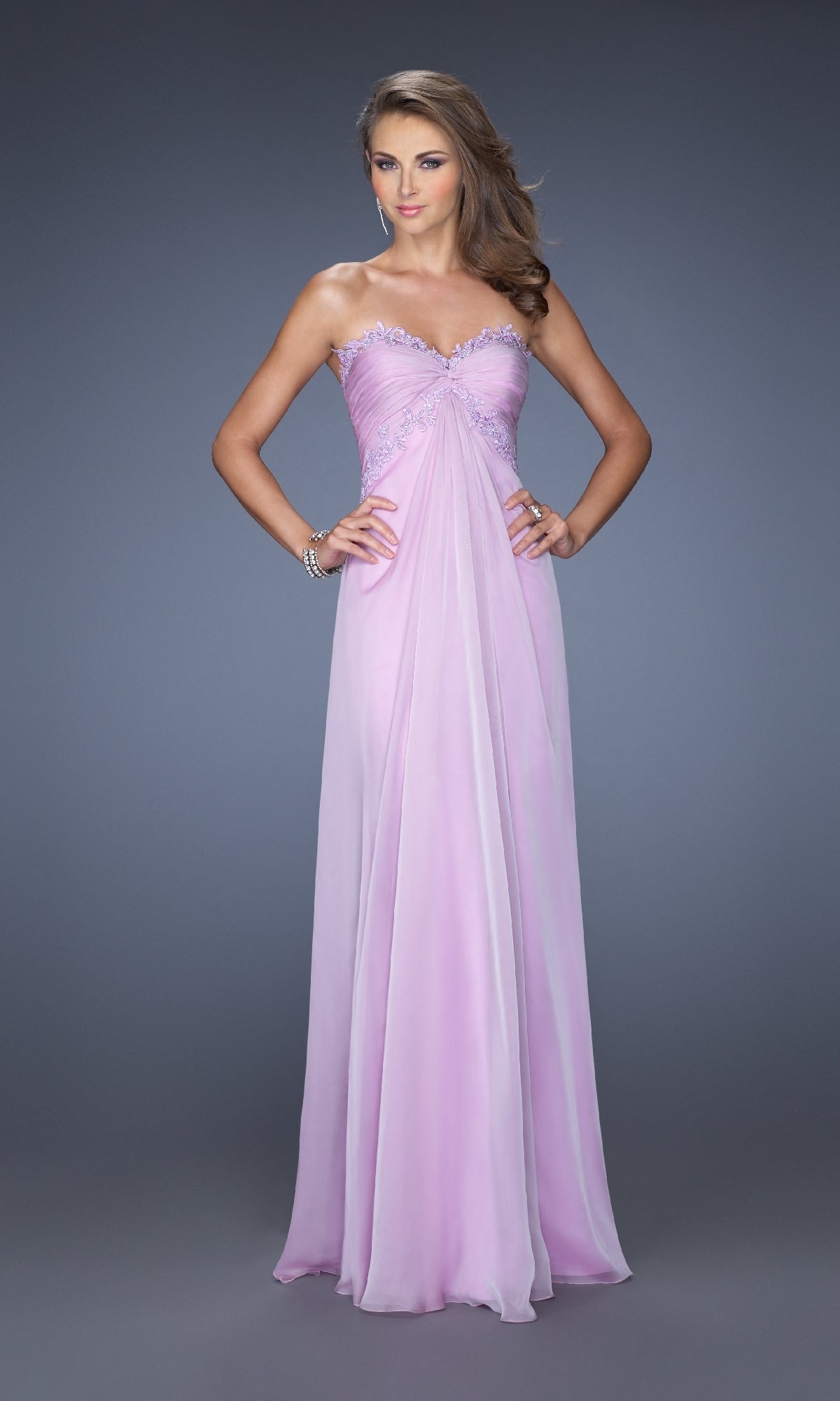A woman poses gracefully in a floor-length light pink La Femme 20042 strapless long A-line prom dress with beaded detailing, set against a plain gray background.