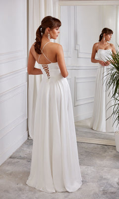 A woman wearing the Aerie Couture 2005 long white dress stands in front of a mirror in a white-walled room with a potted plant.