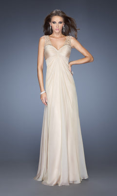 A woman models the La Femme Dress 20122, a floor-length, sleeveless beige chiffon gown with embellished straps and a draped bodice, set against a plain gray background.