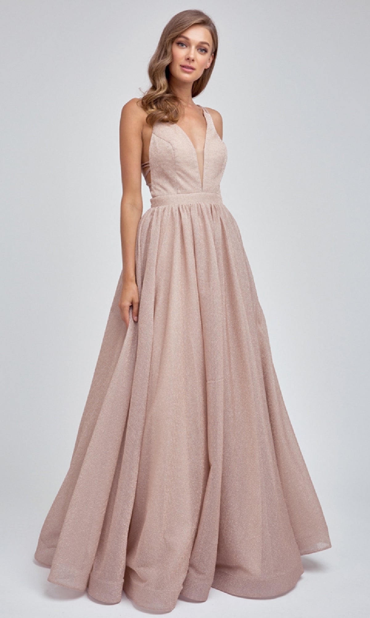 Woman wearing the Juliet 201 Long Prom Dress, a floor-length blush pink gown with a sleeveless deep V-neckline and elegant A-line skirt, standing against a plain light background.