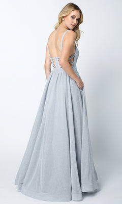 A woman in the Juliet 201 Long Prom Dress, a light gray floor-length gown with an a-line skirt, lace-up detailing, and a cut-out back, stands and looks over her shoulder.