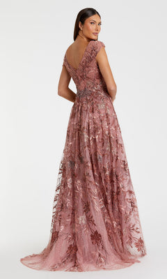 A woman stands facing slightly away, wearing the Mac Duggal 20263 Cap-Sleeve Long Print Prom Dress— a floor-length mauve lace gown with embroidered floral prints and cap sleeves—against a plain white background.