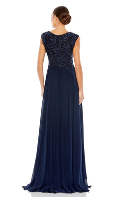 A woman with hair in a low bun faces away, wearing the Mac Duggal 20264 Beaded-Bodice Long Formal Dress in navy blue, featuring cap sleeves, a beaded v-neck bodice, and a flowing chiffon skirt.