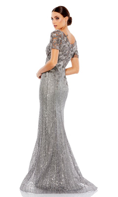 Woman poses in the Long Formal Dress 20282 by Mac Duggal—a silver, floor-length gown with short sleeves and a v-neckline—glancing over her shoulder against a white background.