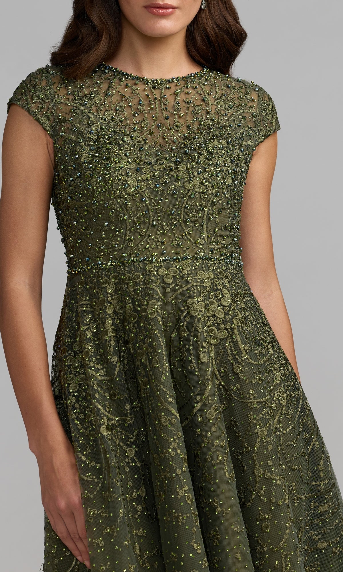 A woman wearing the Tea Length Lilac Party Dress by Mac Duggal (Style 20338), featuring cap sleeves and intricate beadwork and embroidery, stands against a plain gray background.