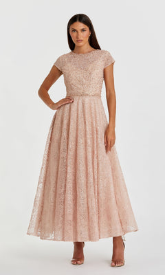 A woman stands against a white background in the Cap Sleeve A-Line Formal Dress: Mac Duggal 20371, featuring a blush pink hue, floor-length skirt, cap sleeves, and an embellished bodice.