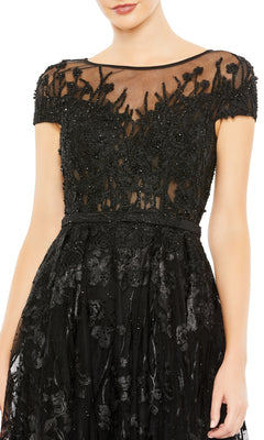 A woman in the Mac Duggal 20405 Short-Sleeve Long Formal Dress, featuring black floral lace and beaded embellishments on a sheer bodice.