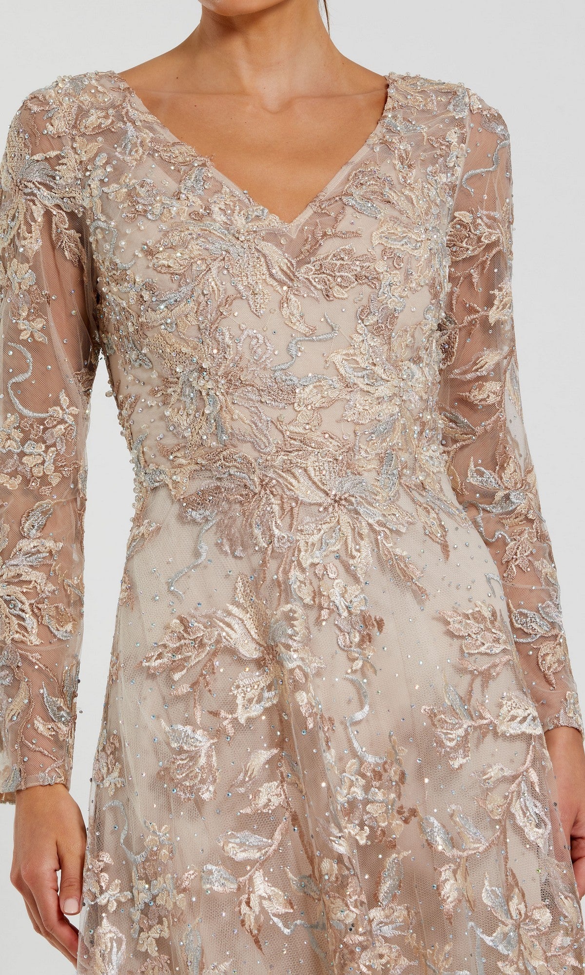A woman wears the Mac Duggal 20409, a long formal dress in light beige with lace embroidery, long sleeves, a V-neckline, intricate floral details, and silver sequins.