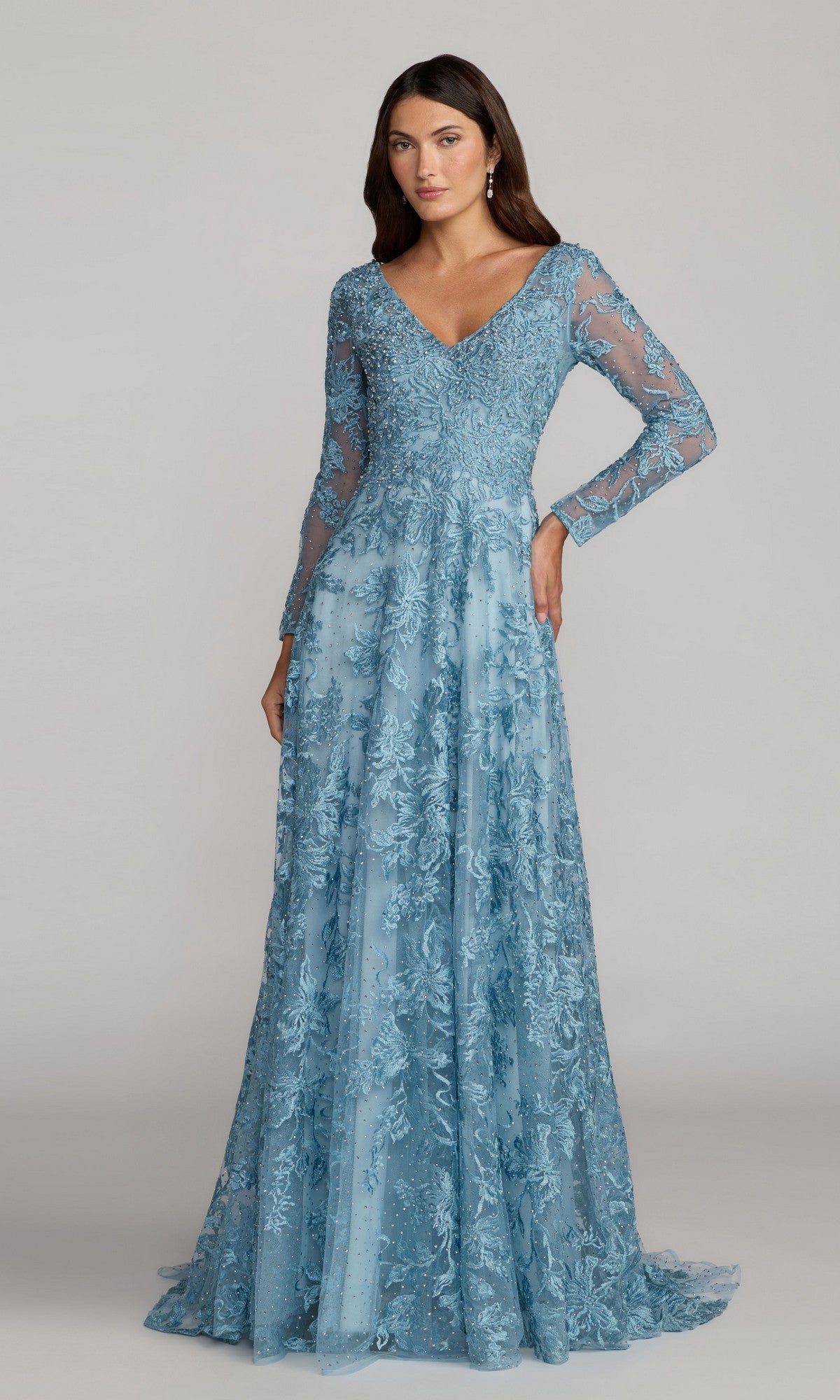 A woman models the Mac Duggal 20409 Long Sleeve Lace Formal Gown in French Blue, featuring a floor-length embroidered lace design and V-neckline—an elegant choice for a mother of the bride.