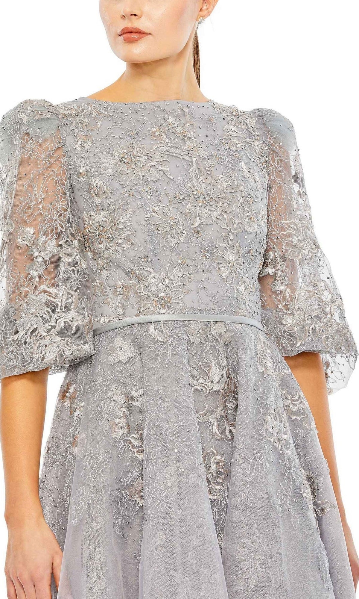A woman models the Long Formal Dress 20418 by Mac Duggal, featuring a light gray high neck, sheer puff sleeves, and delicate floral embroidery, shown from the shoulders to mid-thigh.