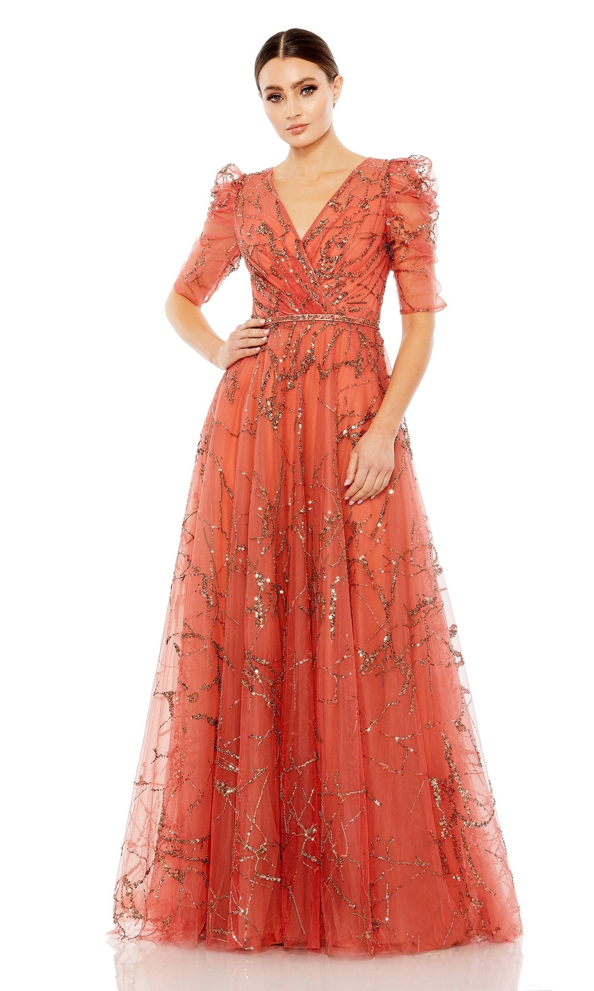 A woman poses against a plain white background wearing the Long Formal Dress 20428 by Mac Duggal, an A-line coral gown featuring puffed sleeves, a V-neckline, a beaded belt, and metallic sequin embellishments.