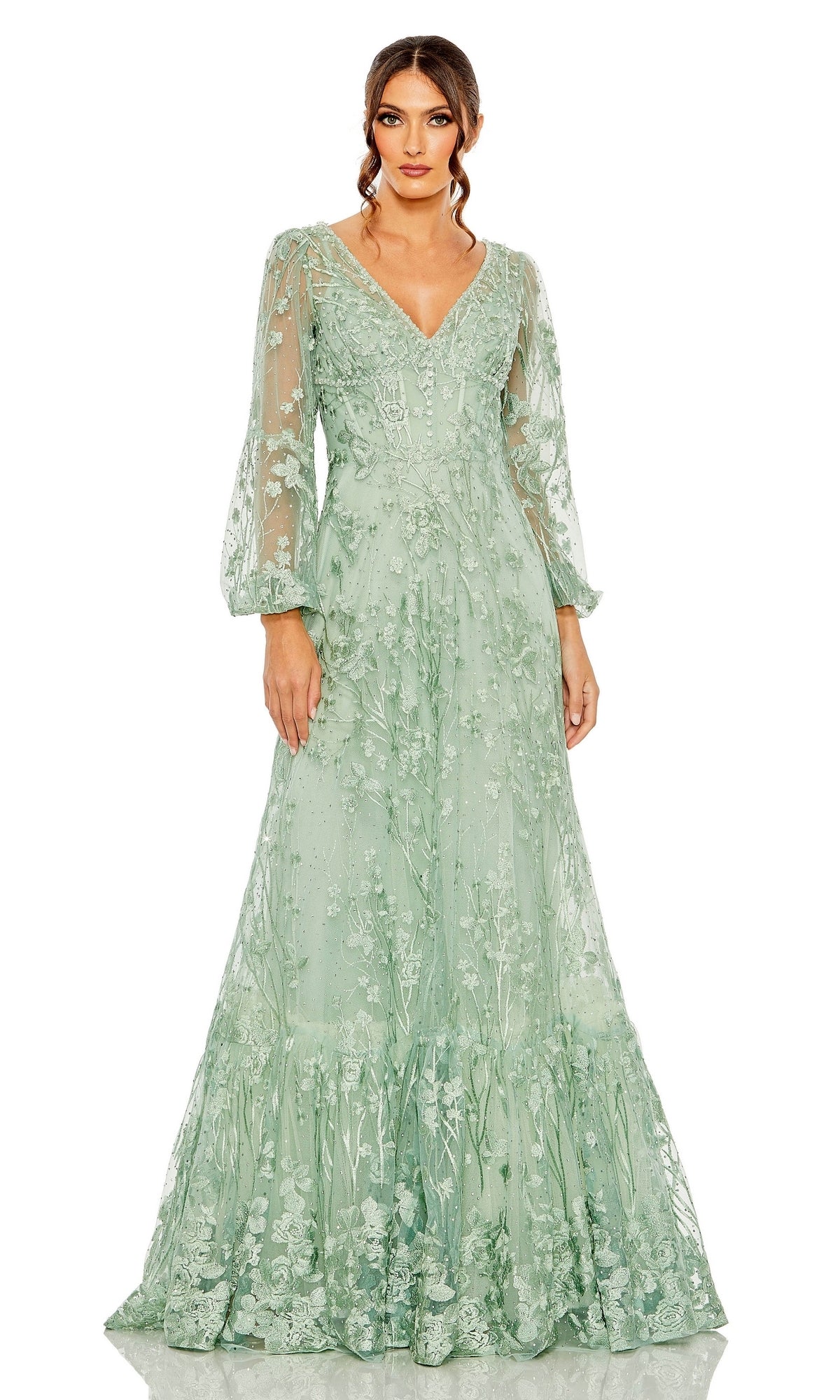 A woman stands facing forward in the Mac Duggal 20430 long sleeve, light green embroidered formal dress with a V-neckline and sheer sleeves.