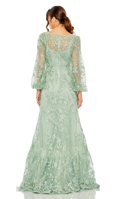 A woman in the Mac Duggal 20430 long sleeve formal dress, featuring sheer light green fabric with floral embroidery and a fitted waist, stands with her back to the camera.