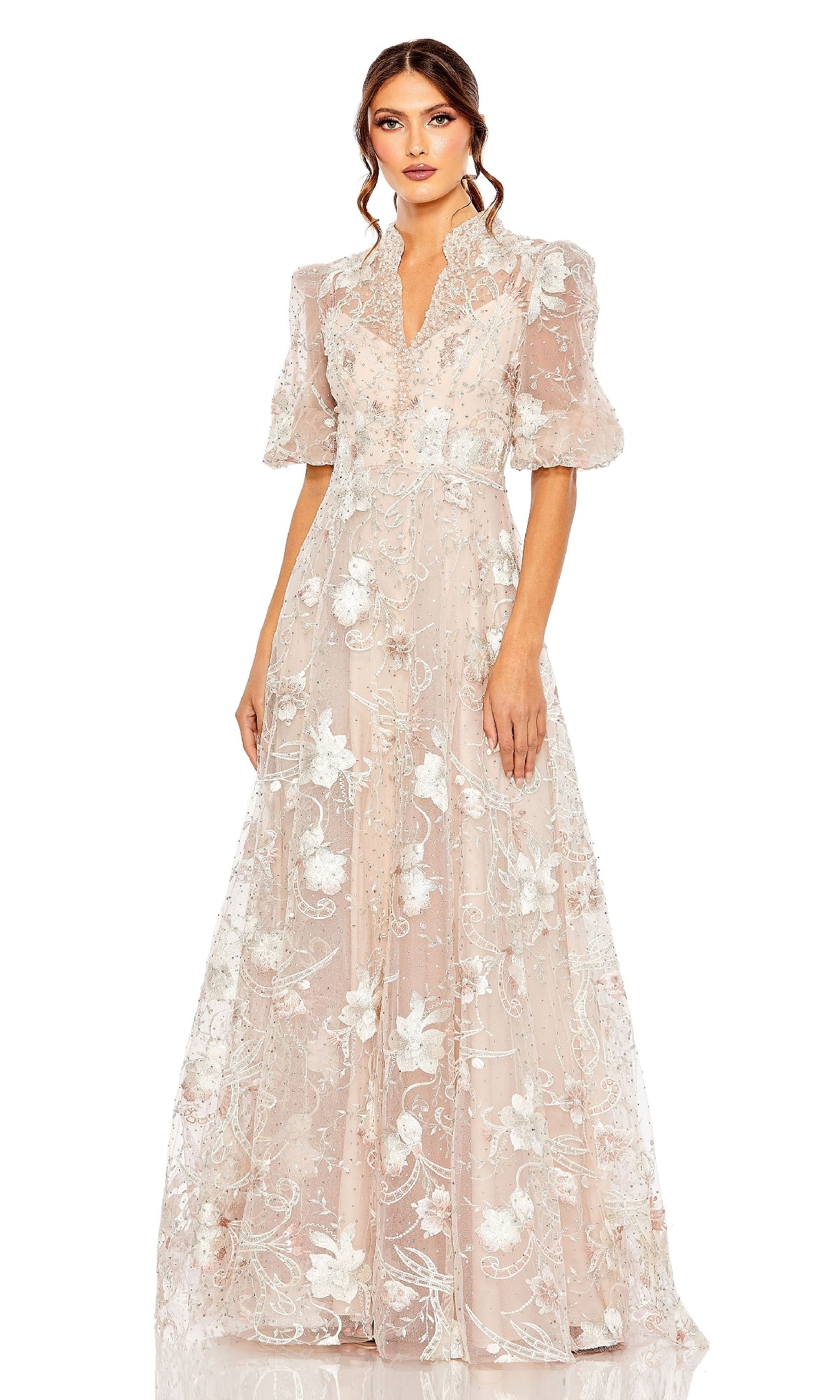 A woman stands against a plain background wearing the Mac Duggal 20452 long formal dress in sheer blush pink with white floral embroidery and puff short sleeves.