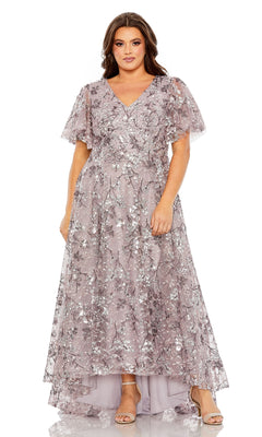 A woman wears the Mac Duggal 20473 long plus-size formal dress in lavender, featuring a floral sequin pattern, flutter sleeves, and a V-neckline. She stands facing forward with a neutral expression.