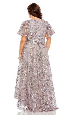 A woman stands facing away, wearing the Mac Duggal 20473: a long plus-size formal dress in lilac with silver floral patterns and short flutter sleeves.