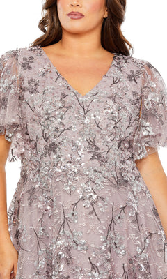 A person wearing the Mac Duggal 20473 long plus-size formal dress in light mauve, featuring floral lace, short flutter sleeves, and silver sequin embroidery.