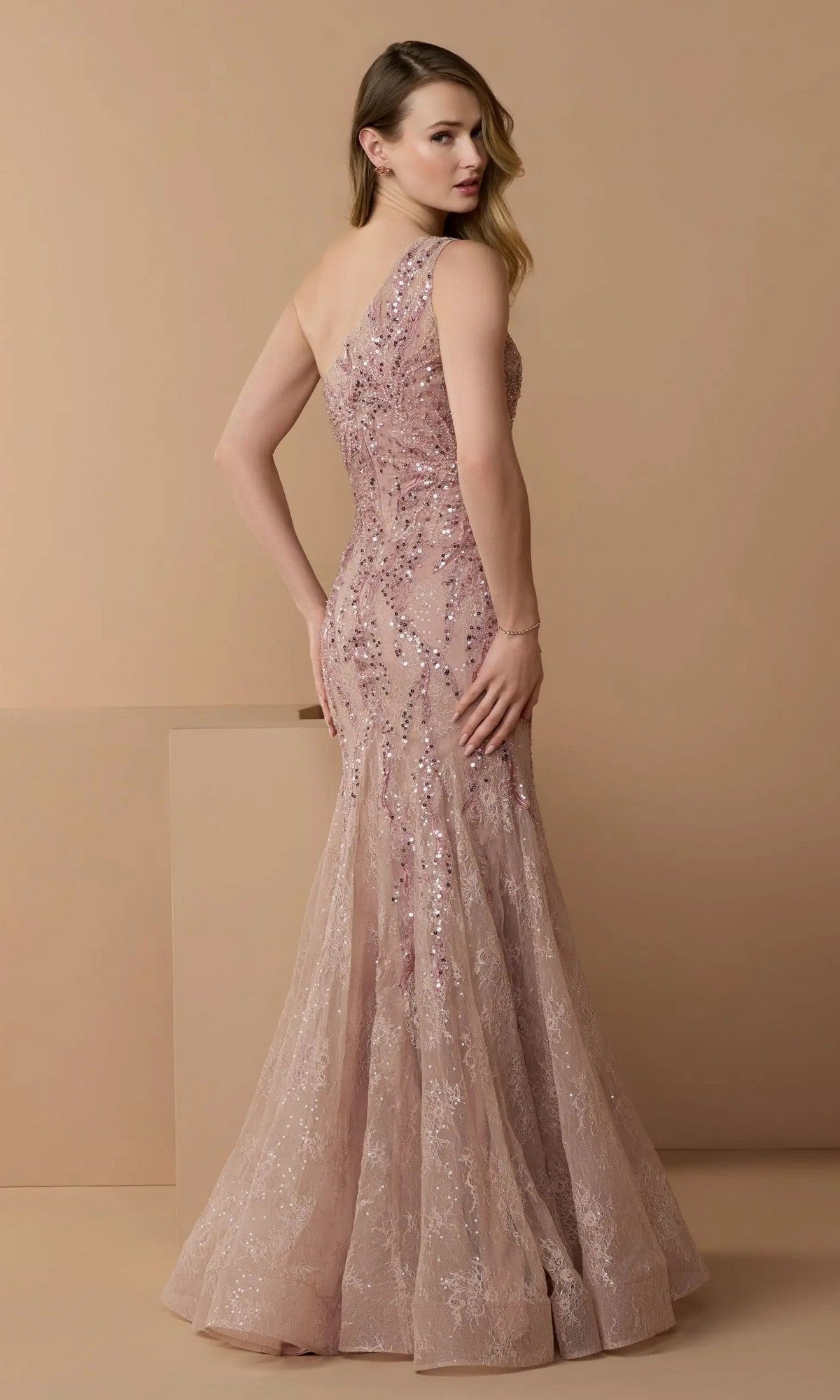 A woman models the Mac Duggal 20482 long formal dress, a blush one-shoulder mermaid gown with sequins and embellished lace, against a plain beige background.