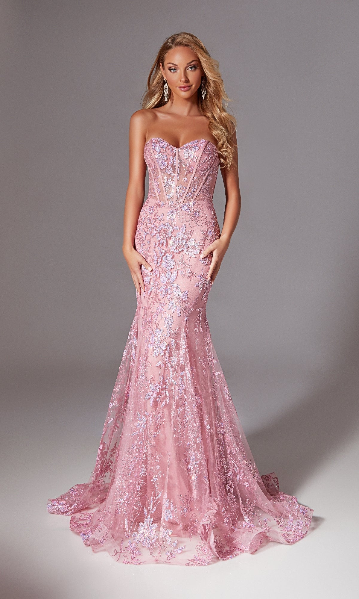 A woman poses against a plain backdrop in the Sparkly Long Mermaid Prom Dress: Aerie Couture 204—a strapless, fitted pink lace gown with floral embroidery, sheer panels, a slight train, and elegant mermaid styling.