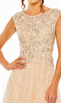 A woman wearing the Mac Duggal 20501 long formal dress—a sleeveless, light beige gown with silver beading, floral embroidery, and a lace overlay—stands with her hand on her hip.