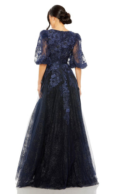 A woman is shown from the back against a white background wearing the Long Formal Dress 20506 by Mac Duggal, featuring midnight blue lace with sheer sleeves and floral embroidery in an elegant A-line silhouette.
