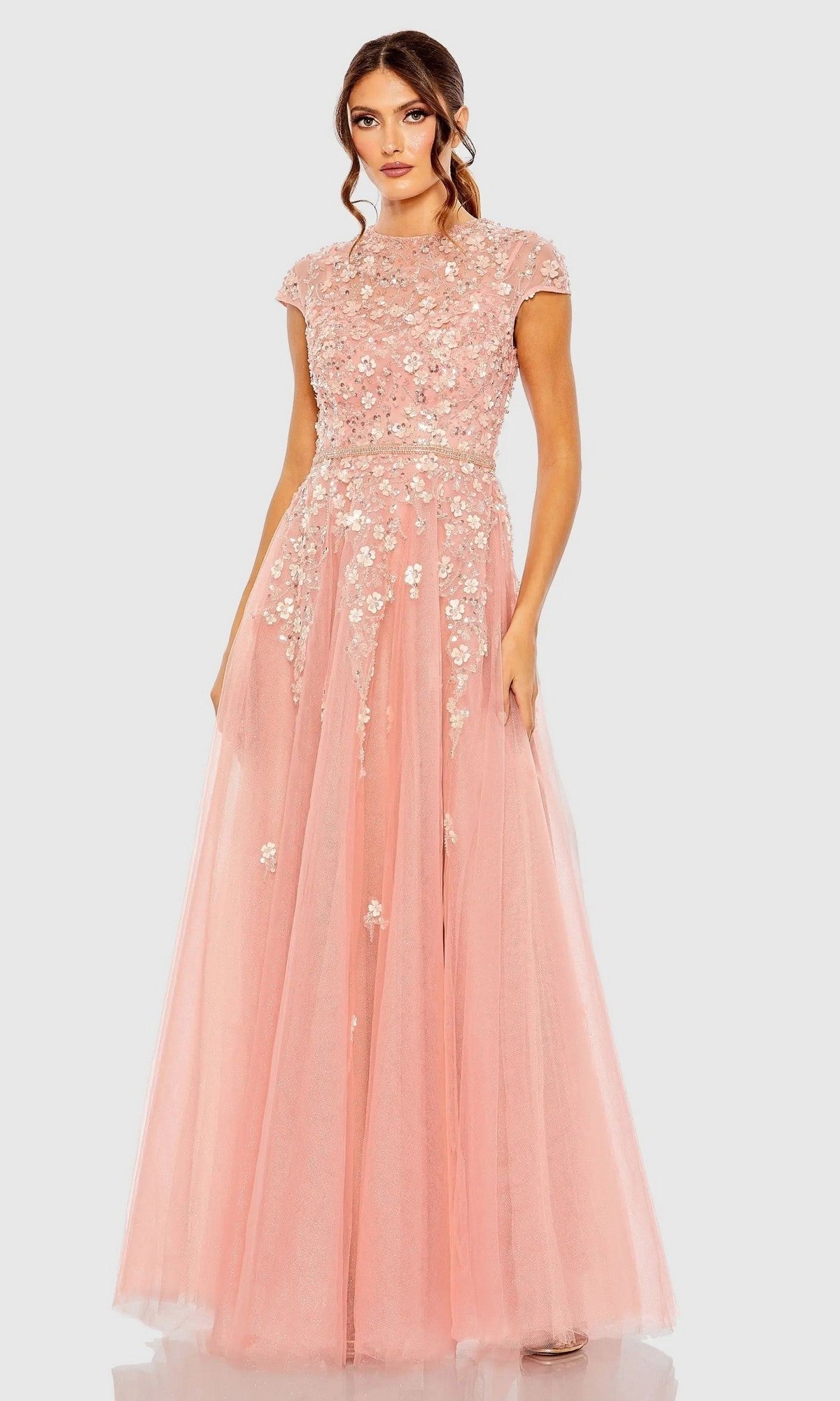 A woman wears the Mac Duggal 20511 Long Formal Dress in rose, featuring short sleeves, floral appliqué details, and a tulle floor-length skirt, standing against a plain light background.