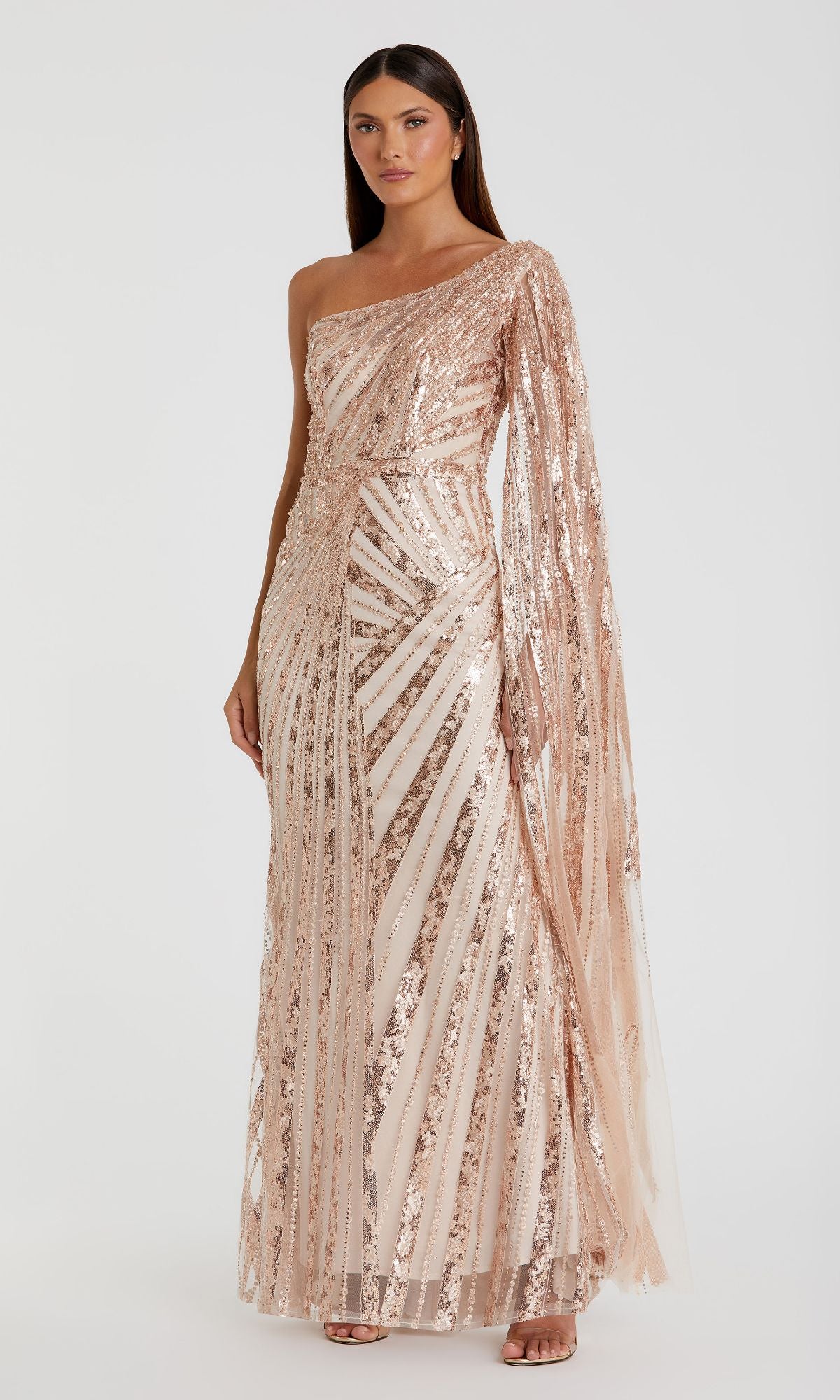 A woman wears the Mac Duggal 20528, a one-shoulder long prom gown with rose gold sequins, sheer fabric, and geometric patterns.
