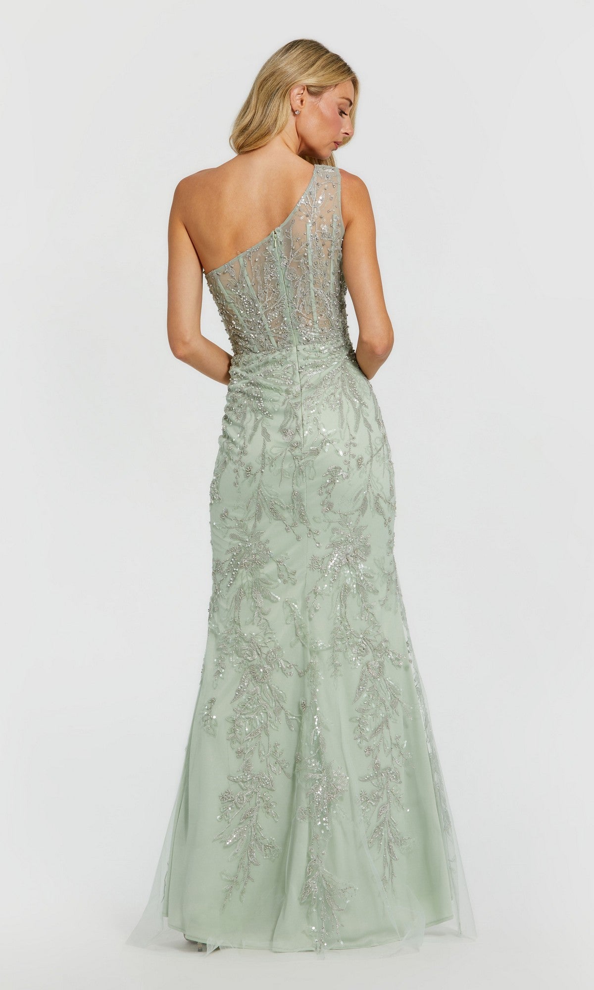 A woman faces away against a plain background, wearing the Long Formal Dress: Mac Duggal 20543—an elegant pale green one-shoulder evening gown with sheer, embellished detailing.