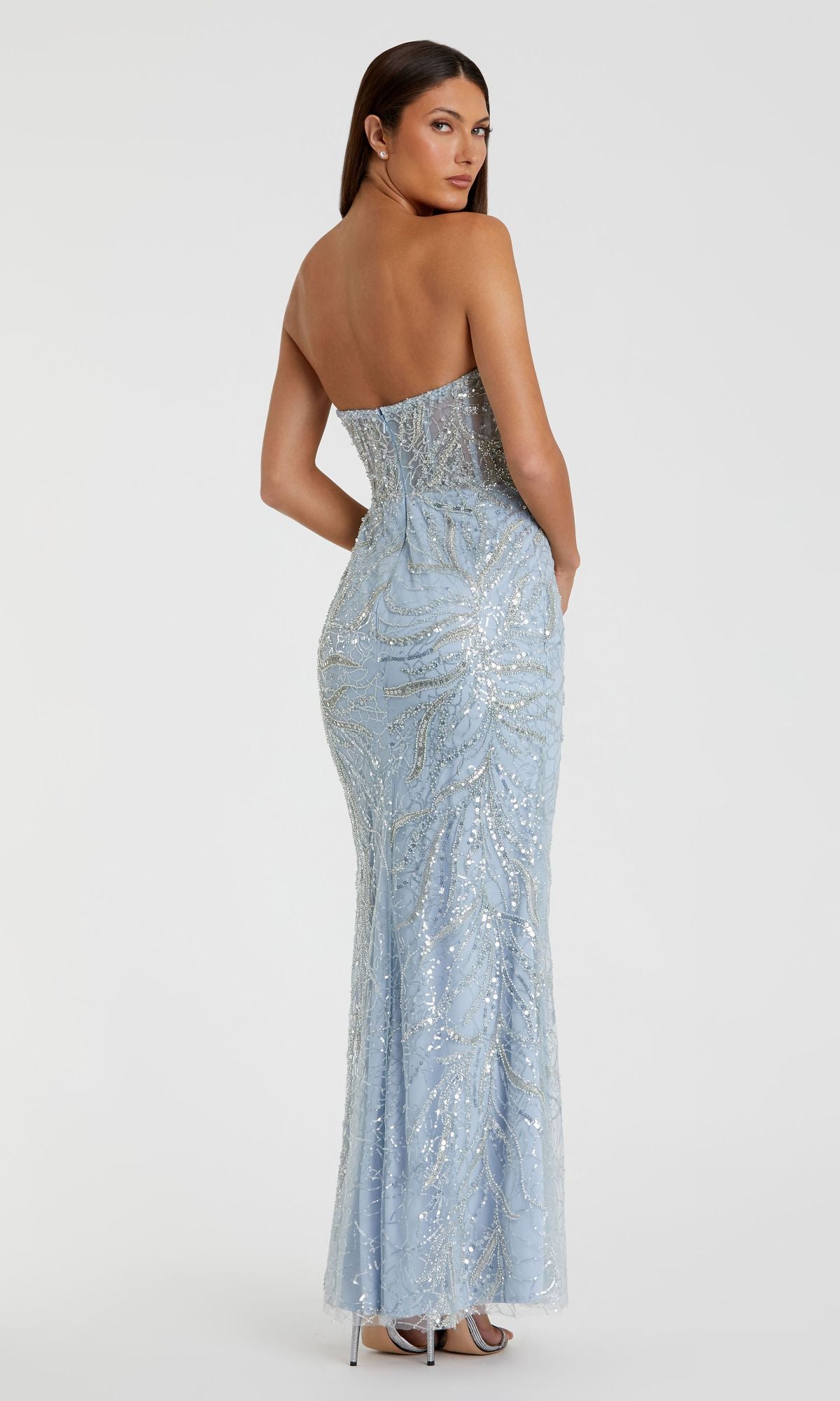 A woman faces away from the camera in a strapless, light blue, beaded Mac Duggal 20544 prom dress, highlighting its elegant design against a plain white background.