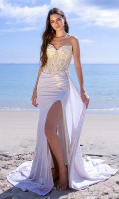 A woman wearing the Amelia Couture 2055 Strapless Corset Prom Gown, featuring an embellished corset and thigh-high slit, stands on a sandy beach with the ocean in the background.