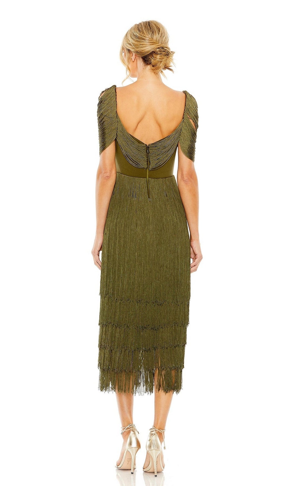 A woman stands facing away, wearing the Short Wedding Guest Dress 20568 by Mac Duggal in olive green with knee-length fringe and metallic high-heeled sandals, her hair in a loose updo.