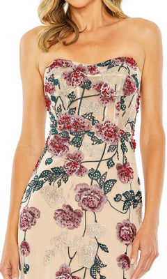 A woman poses confidently with one hand on her hip, wearing the beige Long Formal Dress 20581 by Mac Duggal with red and green floral embroidery.