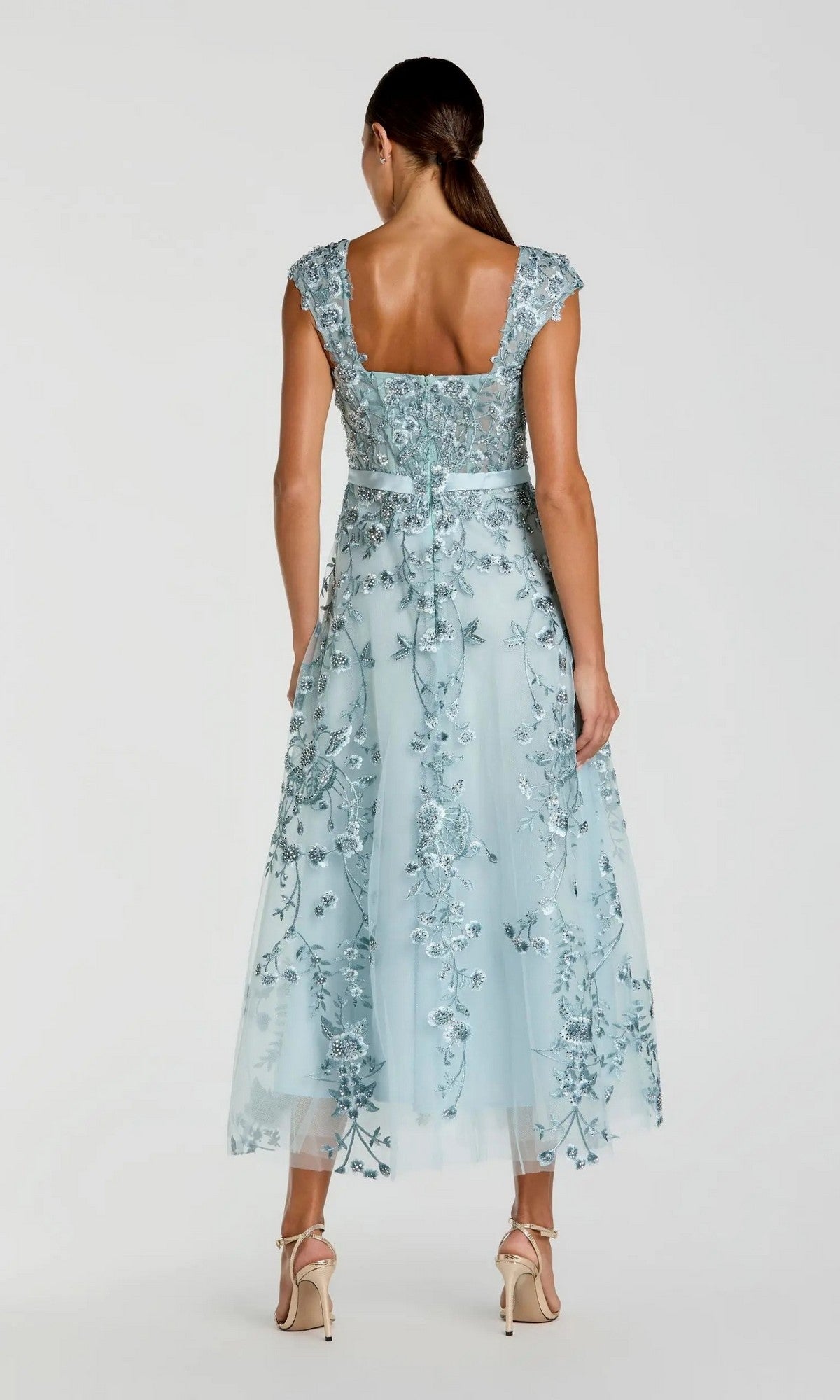 A woman wearing the Mac Duggal 20582 Cap-Sleeve Nude Midi Party Dress with floral embroidery and cap sleeves, standing in high-heeled sandals with her back to the camera.