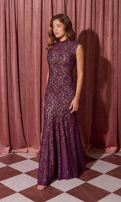 A woman stands on a checkered floor in front of mauve curtains wearing the Eureka 2061 Long Lace Formal Dress, a sleeveless purple evening gown.