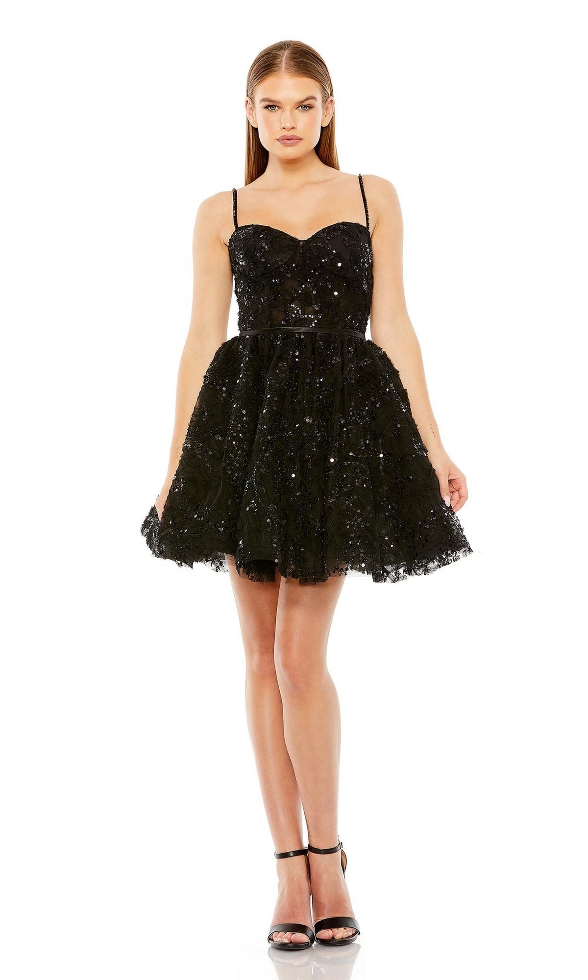 A woman faces forward in the Short Black Beaded Hoco Dress: Mac Duggal 20641, featuring a sweetheart neckline, spaghetti straps, flared skirt, and paired with black high-heeled sandals.