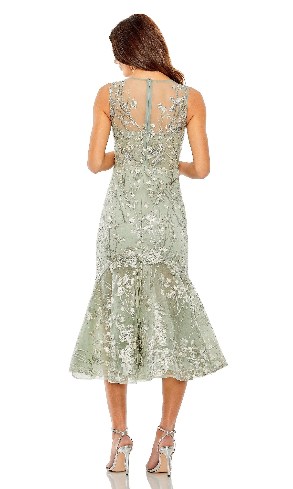 A woman faces away from the camera in the Mac Duggal 20646 Sage Midi Wedding Guest Dress, a sleeveless, knee-length lace dress with floral embroidery, paired with silver high-heeled sandals.