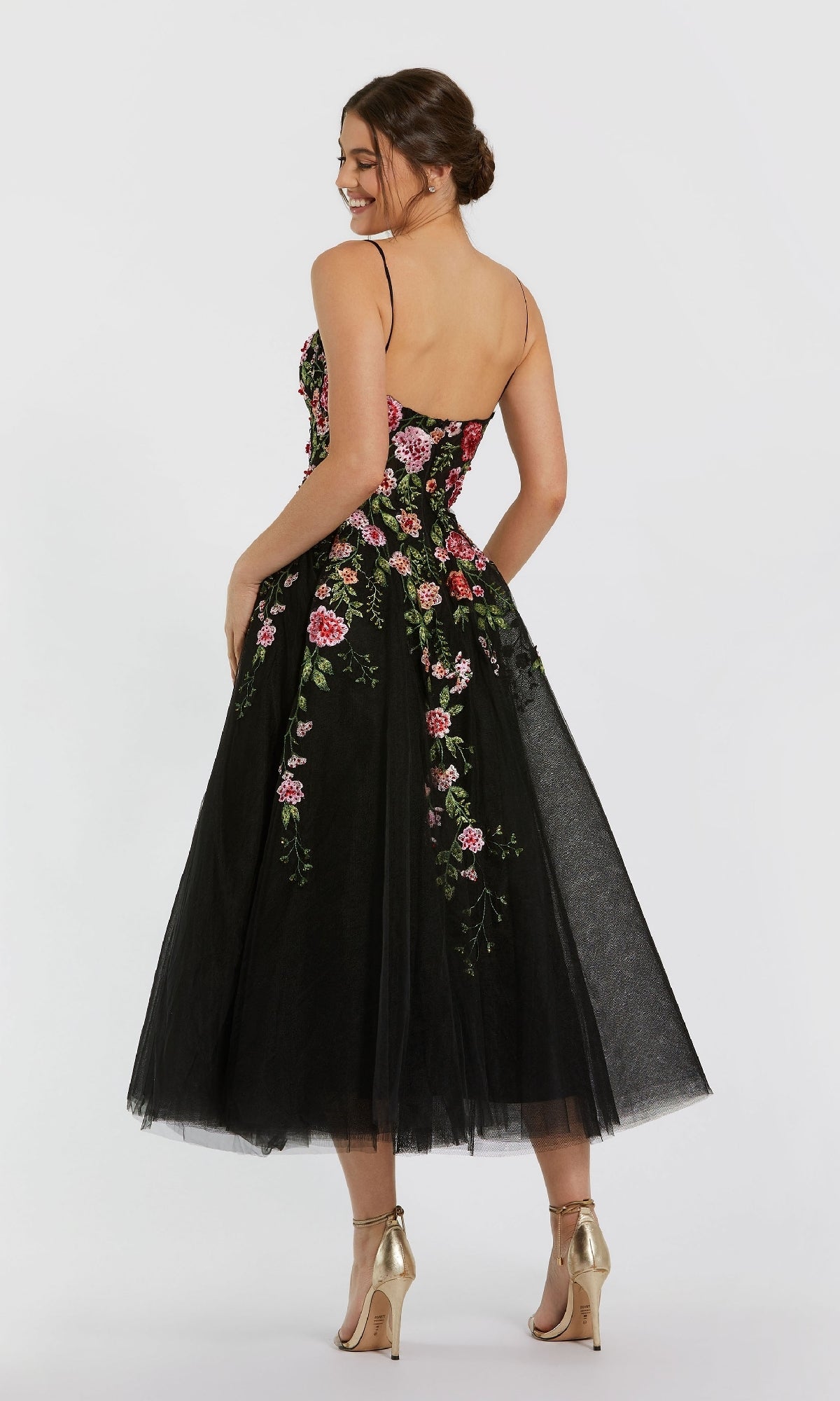 A woman in the Mac Duggal 20651 Floral Embroidered A-Line Midi Dress with spaghetti straps and gold heels stands against a plain background.