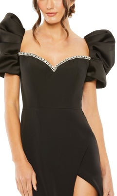 A woman wearing the Long Formal Dress 20687 by Mac Duggal, featuring a fitted black design with puff sleeves, rhinestone-trimmed sweetheart neckline, and thigh-high slit.