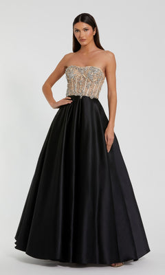 A woman stands against a plain background, wearing the Mac Duggal 20701 strapless black prom ball gown with a beaded sheer corset-style bustier and a full, floor-length A-line skirt.