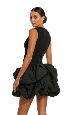 A woman stands facing slightly away from the camera wearing the Mac Duggal 20709 Short Black Bubble Party Dress featuring a sleeveless fitted top and a voluminous mini bubble skirt.