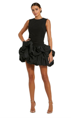 A woman wears the Mac Duggal 20709 short black bubble party dress with a fitted bodice and mini skirt, paired with silver strappy heels.