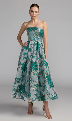 Woman wearing a strapless bronze Mac Duggal 20716 party dress with a flared skirt and gold high heels, standing against a plain gray background.