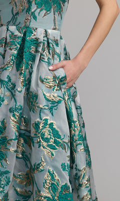 A person in a Mac Duggal 20716 strapless bronze party dress stands with one hand in a pocket.