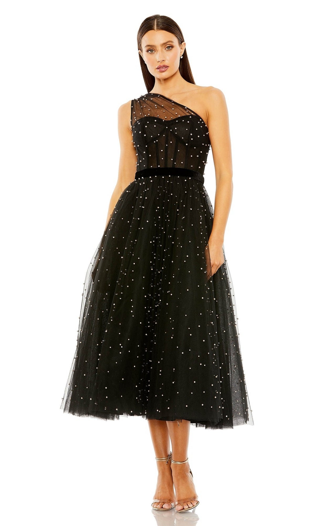 A woman wears the Mac Duggal 20745, a vintage-inspired black midi wedding guest dress featuring a one-shoulder design, tea-length hem, delicate sequins, and sheer overlay, paired with strappy high heels.