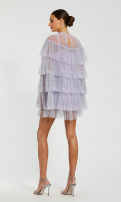 A woman in profile wears the Mac Duggal 20749 short party dress, featuring lavender tulle tiers, sheer sleeves, and silver high heels, posed against a plain background.