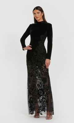 A woman models the Mac Duggal 20746, a long black velvet formal dress featuring floral embroidery and a sheer skirt, posed against a plain white background.