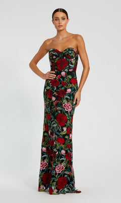 A woman stands gracefully against a plain light backdrop in the Mac Duggal 20757 Long Print Formal Evening Gown, featuring bold red and pink floral prints on a dark background.