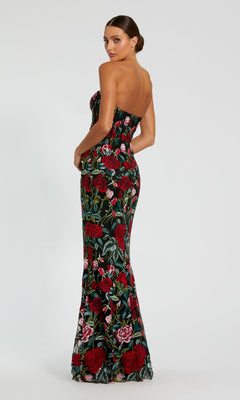 A woman in the Mac Duggal 20757 Long Print Formal Evening Gown, featuring a strapless floral design with red and green accents, stands against a plain light background, looking over her shoulder.