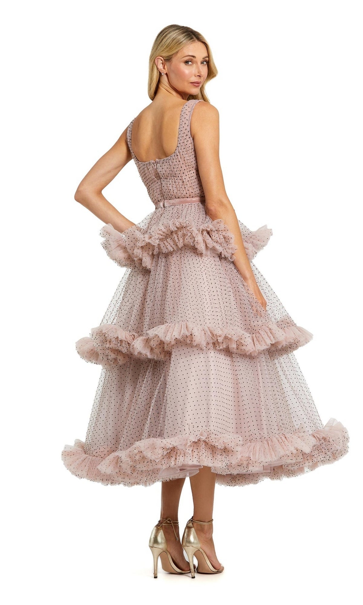 A woman, seen from behind in high-heeled sandals, wears the sleeveless, tiered Pink Midi Wedding Guest Dress: Mac Duggal 20776, featuring blush pink polka dots and ruffle details.